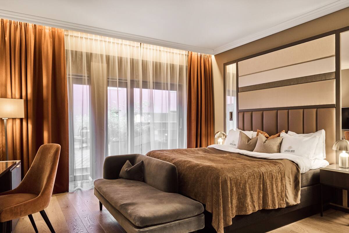 A hotel room with a large bed, a sofa, a desk, and a window with curtains.