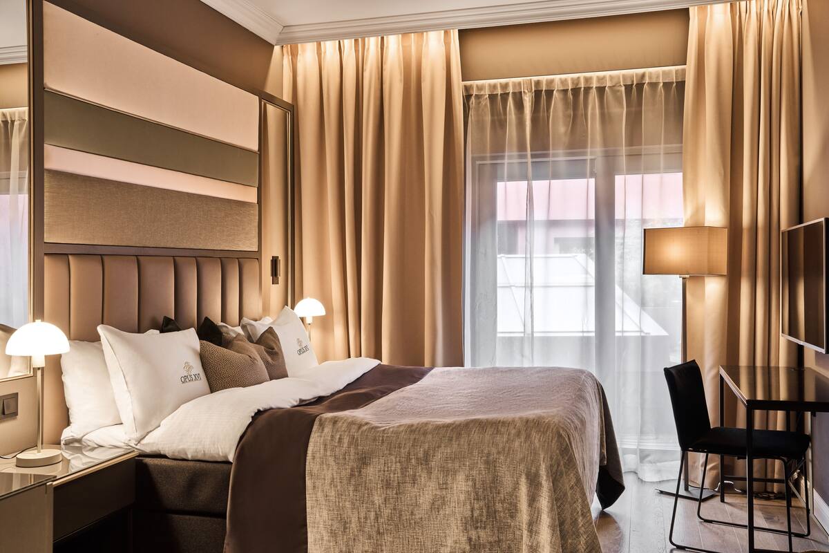 A hotel room with a large bed, a desk, a chair, and a TV.