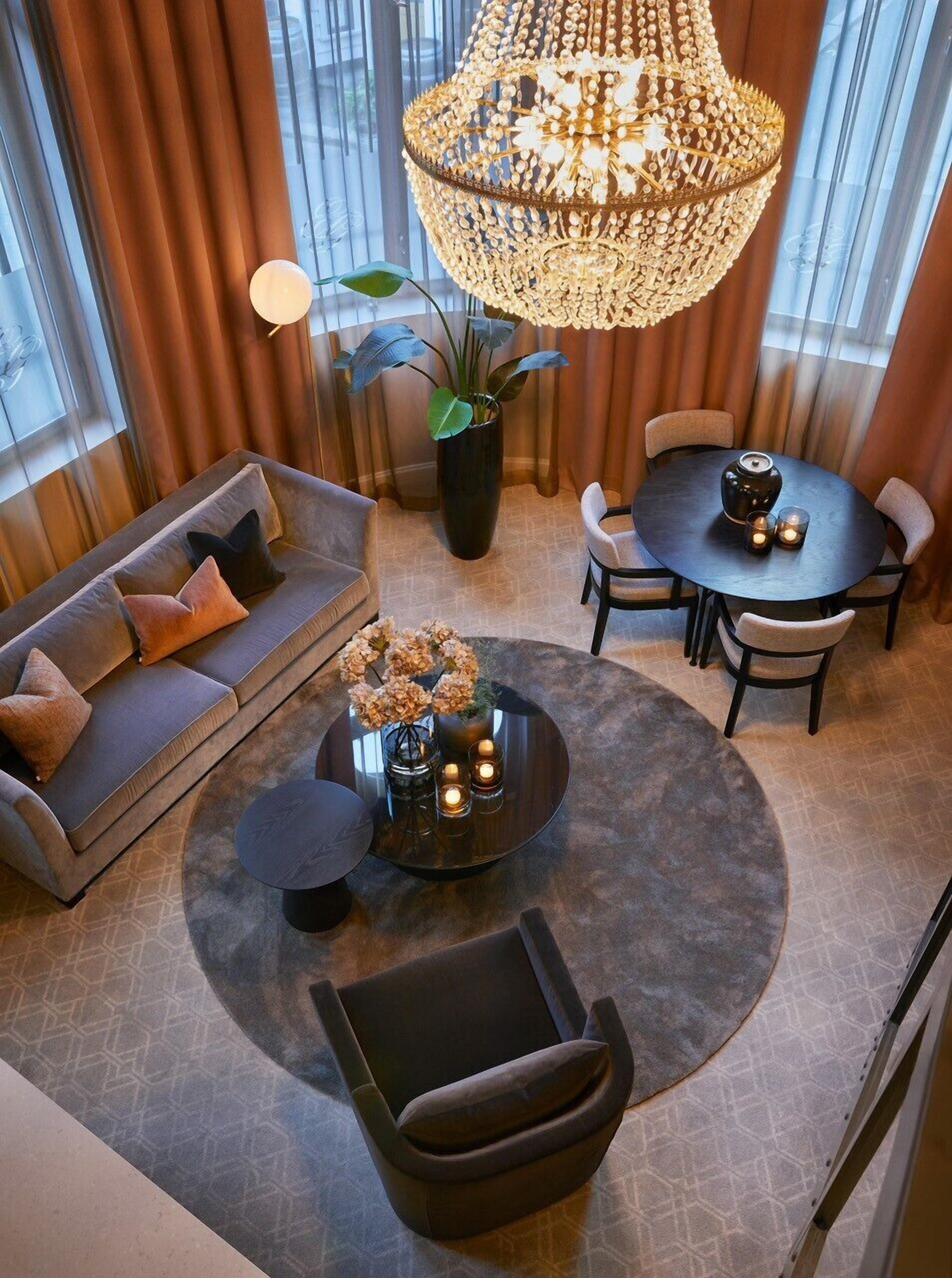 A modern living room with a round coffee table, sofa, and chairs, a large chandelier, and a potted plant.