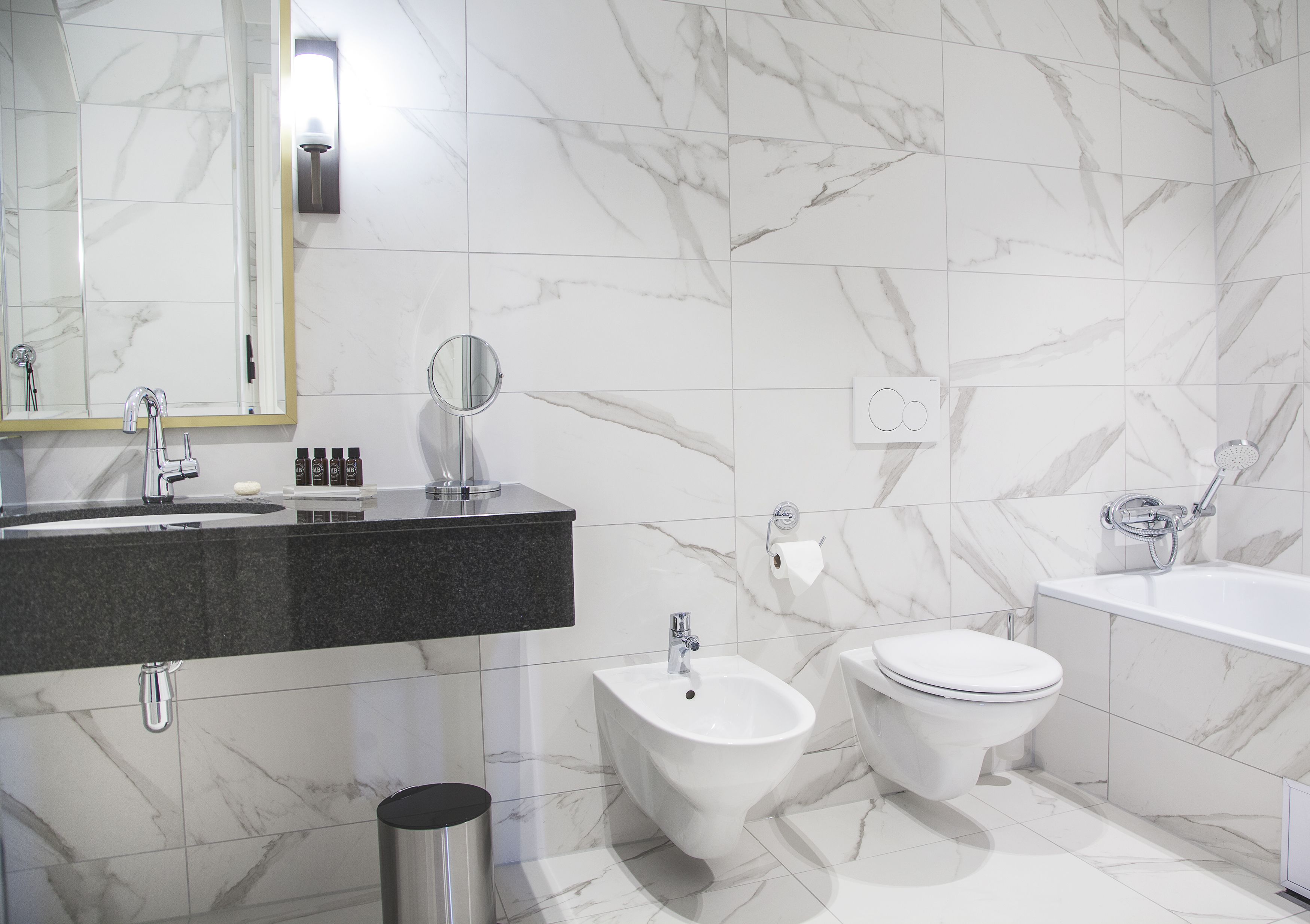 A modern bathroom with a marble backsplash, a bidet, a toilet, and a bathtub.