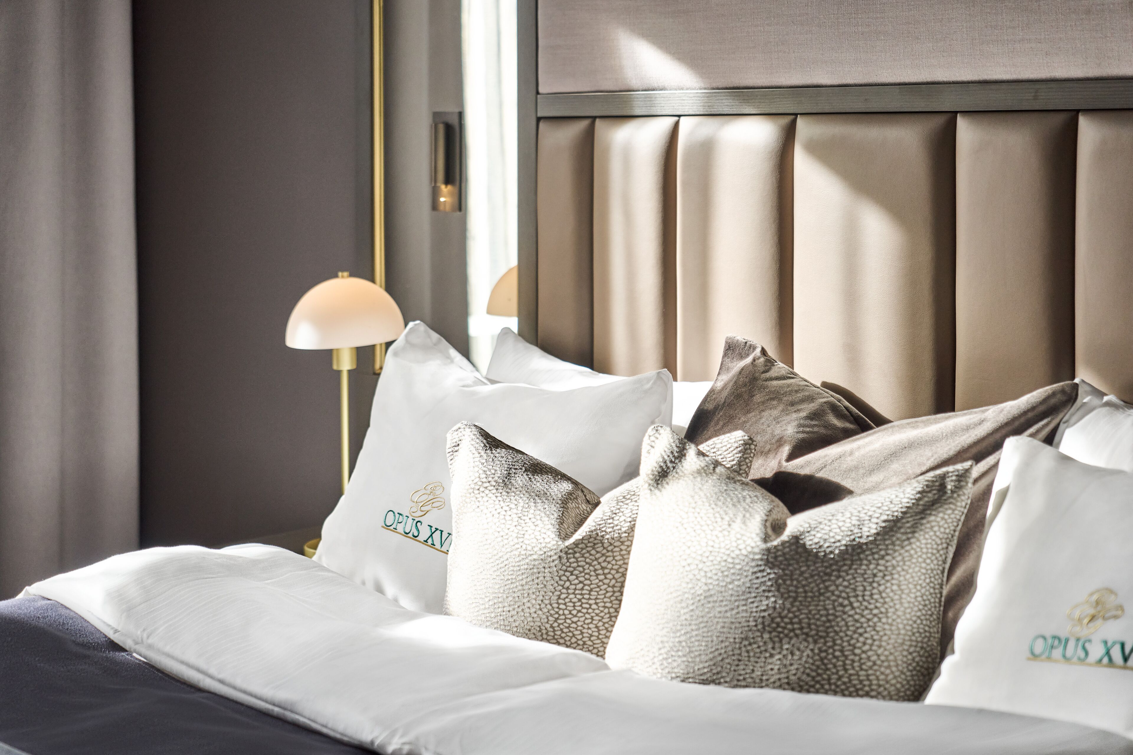 A neatly made bed with white bedding and decorative pillows, a bedside lamp, and a headboard with vertical slats.