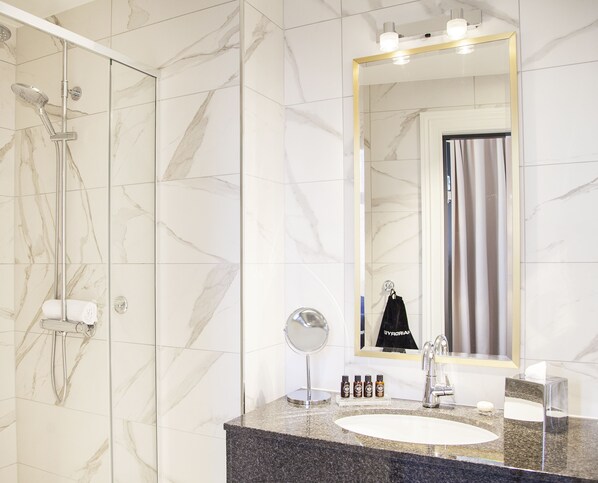 A bathroom with a marble floor, a sink with a mirror, a towel rack, and a shower with a glass door.