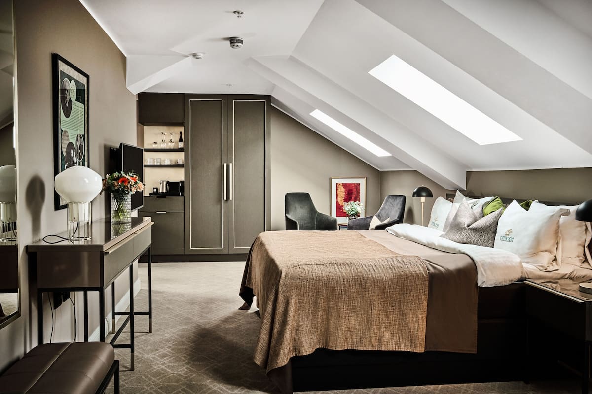 A modern bedroom with a sloped ceiling, a bed with a beige bedspread, a desk with a lamp, and a chair.