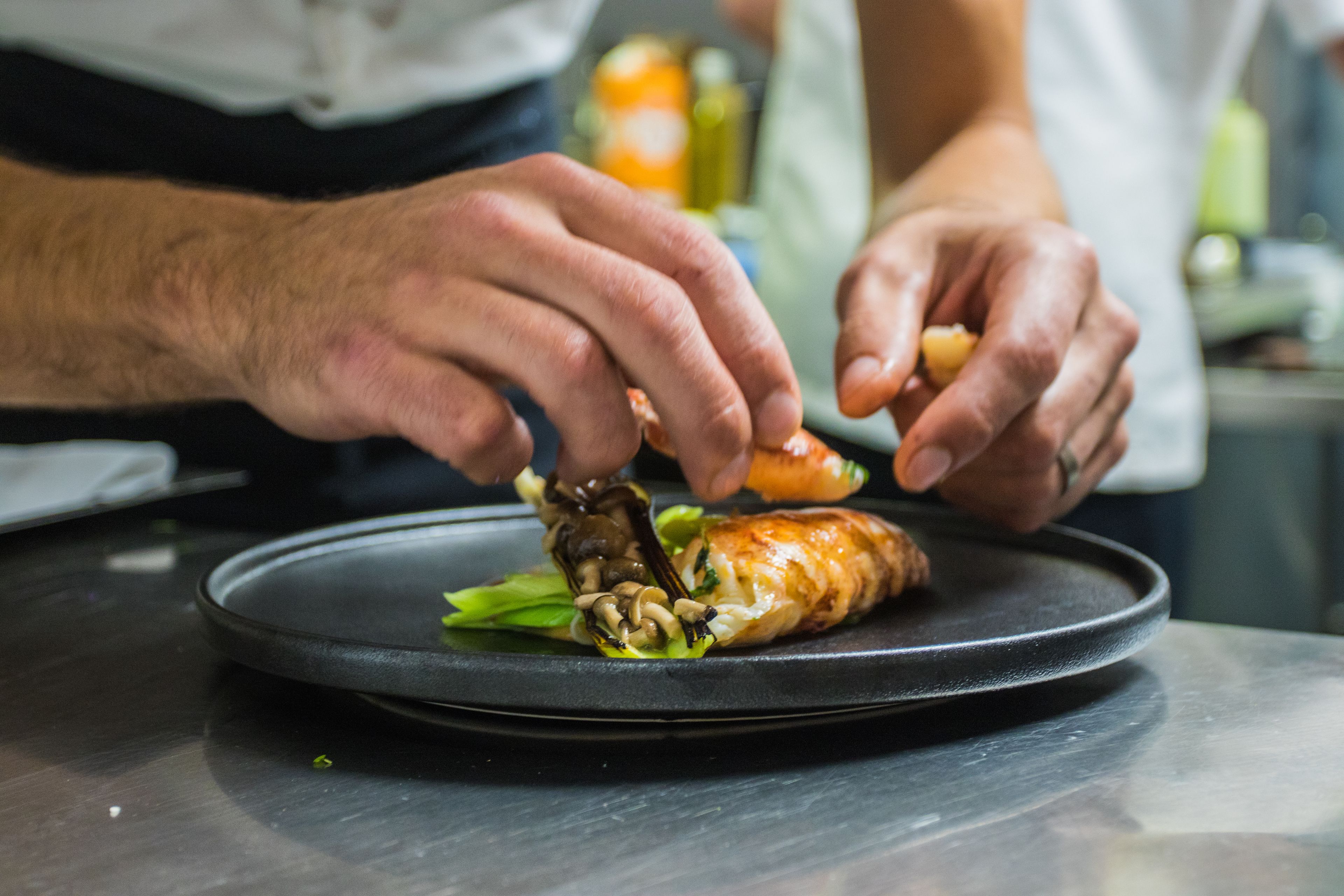 A person preparing food on a black plate with a focus on hands and a pastry.