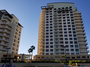 A high-rise residential building with multiple balconies, a flat facade, and a clear sky.