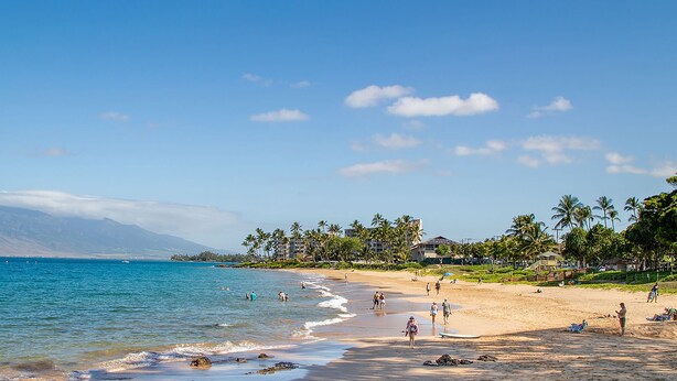 Une plage avec un ciel dégagé, une eau calme et une chaîne de montagnes en arrière-plan.