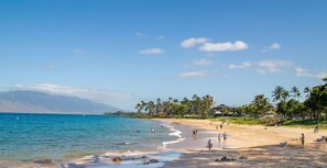 A beach with clear skies, calm waters, and a mountainous backdrop.