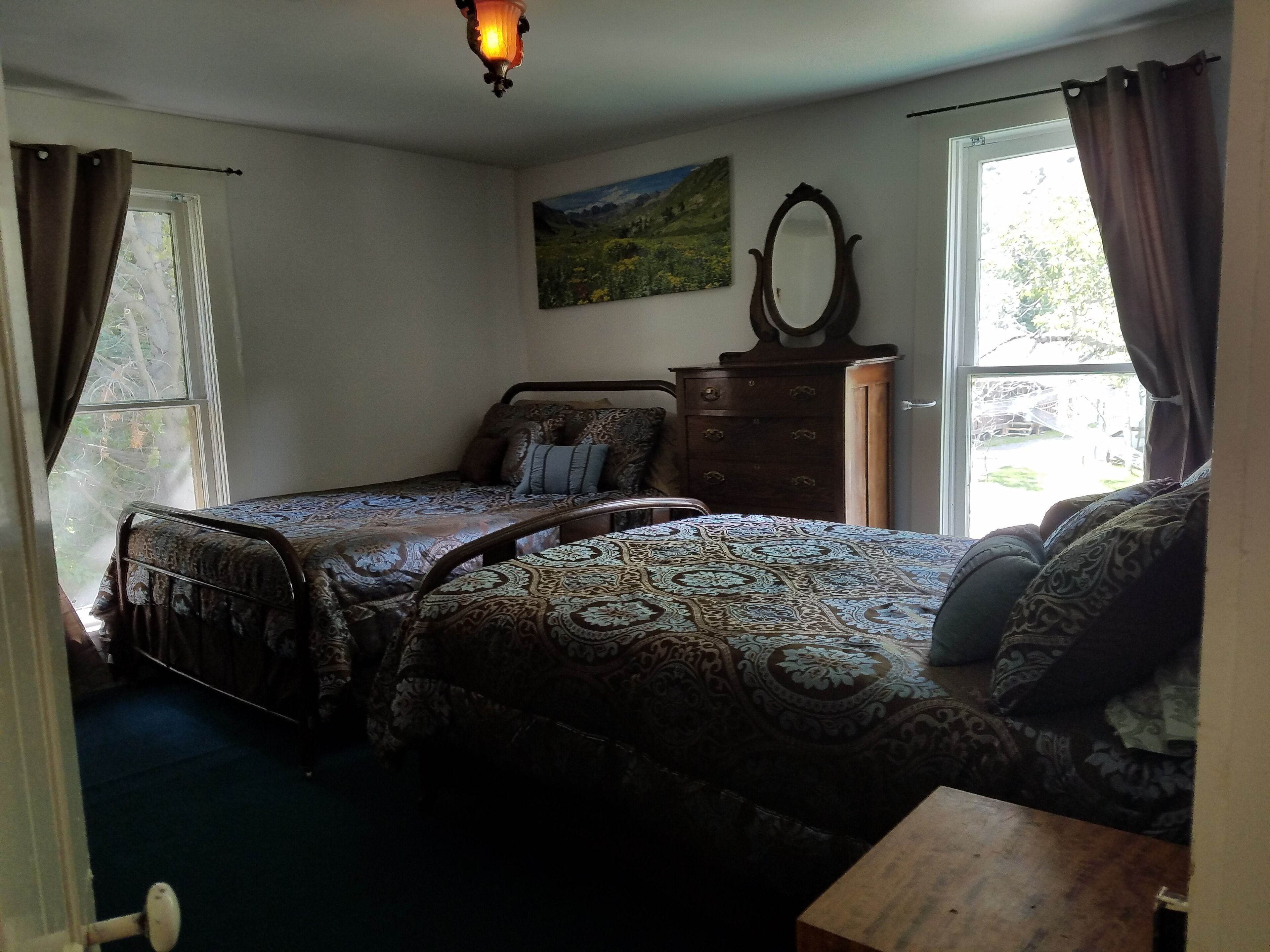 A bedroom with two beds, a dresser, a mirror, and a painting on the wall.