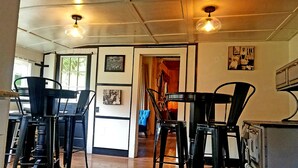 Un comedor con sillas y mesas de metal negro, piso de madera, y una zona de cocina con armarios y estufa.