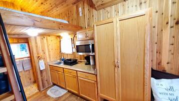 Une petite cabane en bois comprenant un coin cuisine équipé d’un four à micro-ondes et de placards.