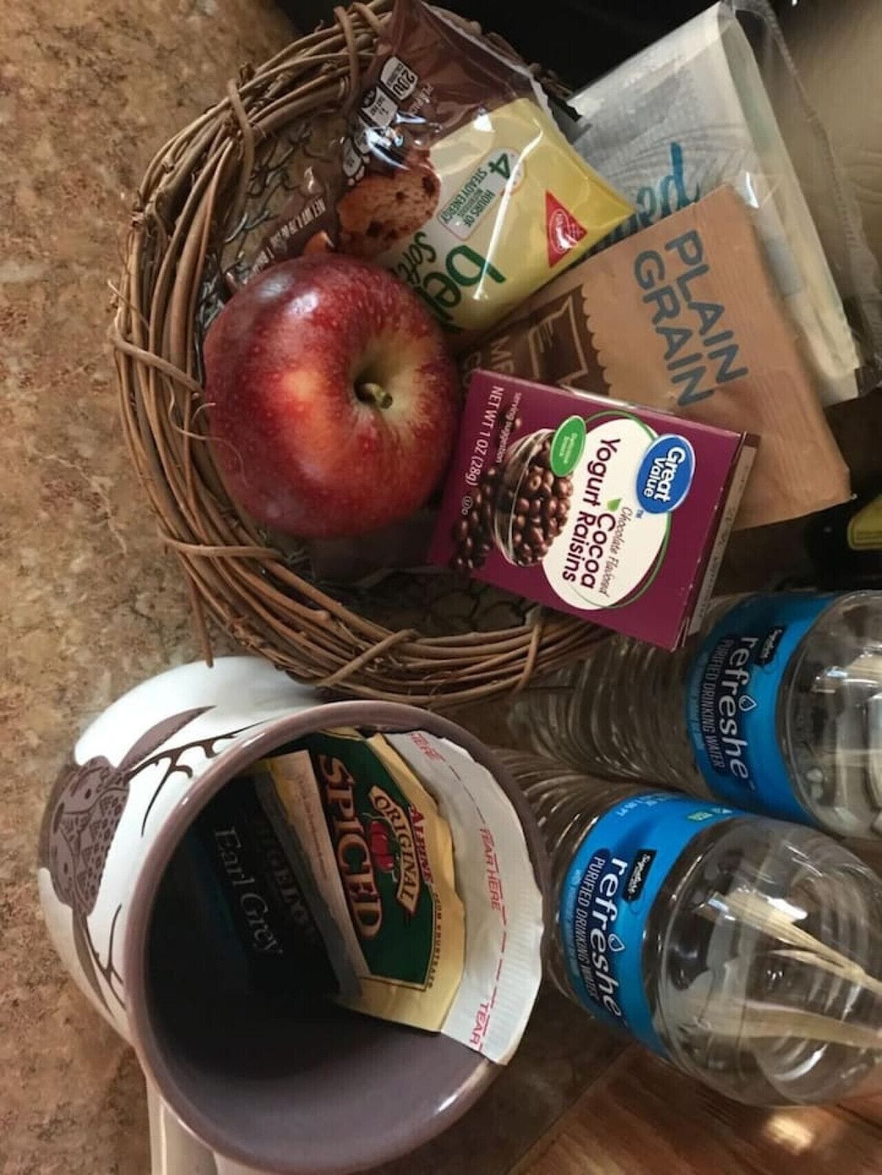 A basket containing an apple, a box of yogurt, a bag of plain grain, and a bottle of water.