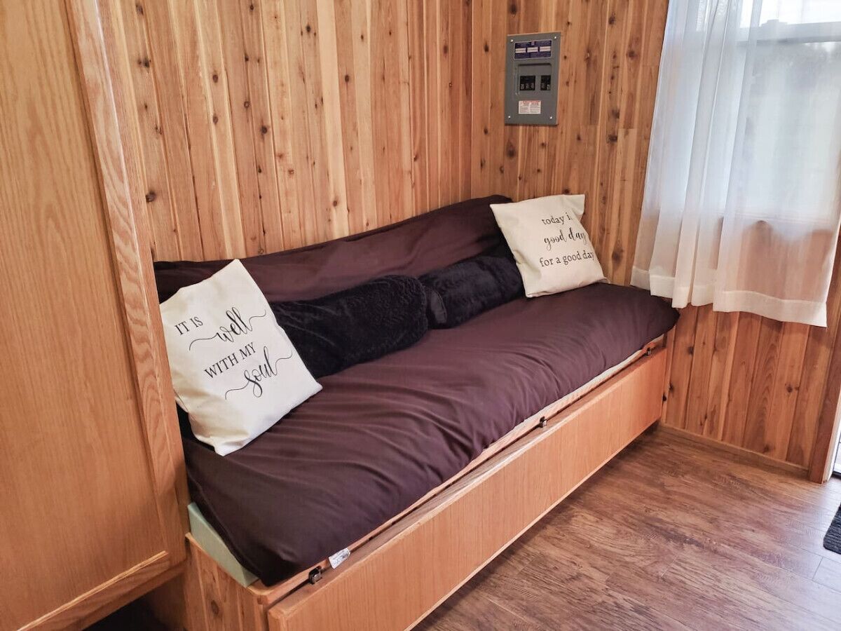 A wooden interior with a built-in sofa bed, two pillows with text, and a power outlet on the wall.