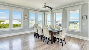 Un espace repas comprenant une table et des chaises, de grandes fenêtres et un ventilateur de plafond.