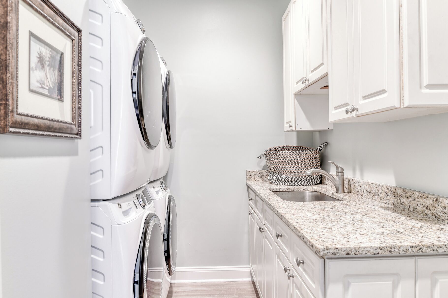 A laundry room with a washing machine and dryer, a sink with a patterned towel, and white cabinetry.