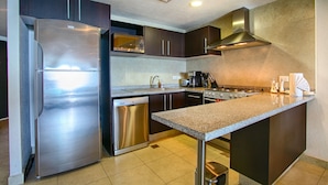 A modern kitchen with stainless steel appliances, dark cabinetry, and a granite countertop. - Pools, Gym & Restaurant | Beachfront 1BR (Puerto Vallarta)