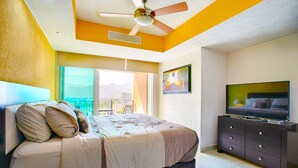A bedroom with a bed, a TV, a ceiling fan, and a window with a view. - Pools, Gym & Restaurant | Beachfront 1BR (Puerto Vallarta)