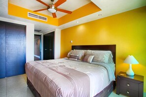 A bedroom with a bed, a nightstand, a lamp, a ceiling fan, and a door. - Pools, Gym & Restaurant | Beachfront 1BR (Puerto Vallarta)