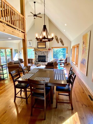 A spacious dining area with a large wooden table and chairs, a fireplace, and a view of the outdoors.