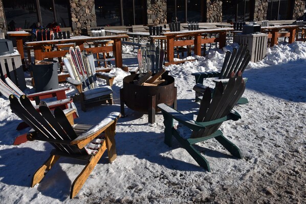 Outdoor seating with snow-covered chairs and tables, a fire pit, and a stone building in the background.