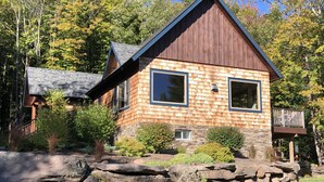 Ein modernes, zweistöckiges Haus mit Steinunterbau, großen Fenstern und Holzfassade.
