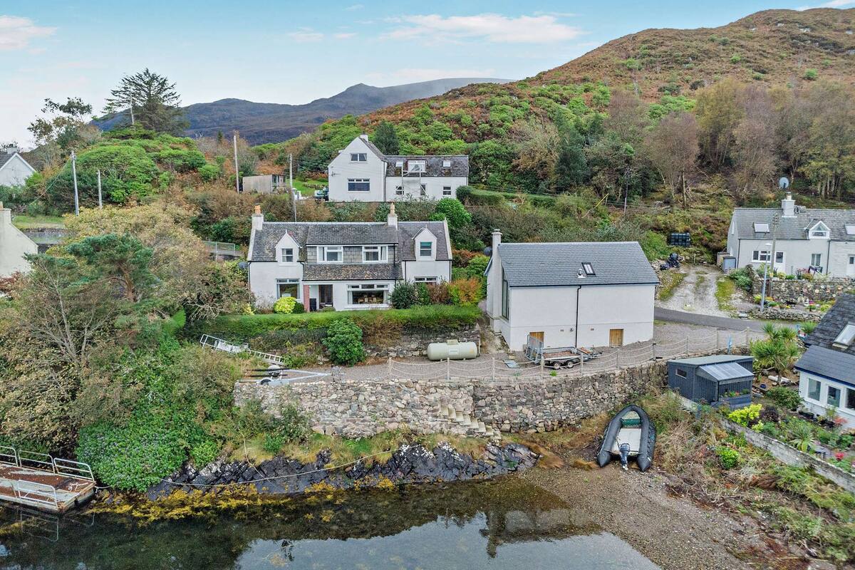 A coastal village with houses, a small body of water, and hills in the background.