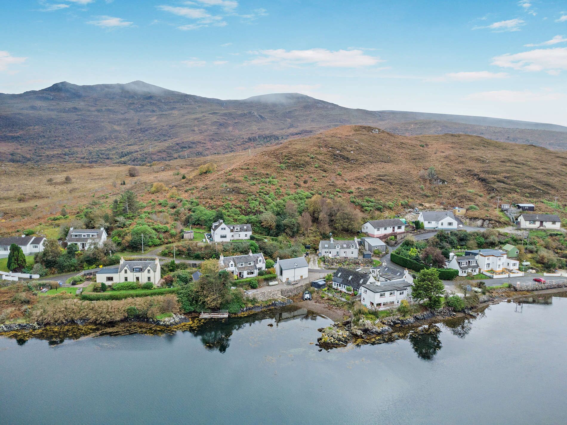 Un pueblo a orillas del lago con casas, un muelle y una montaña al fondo.