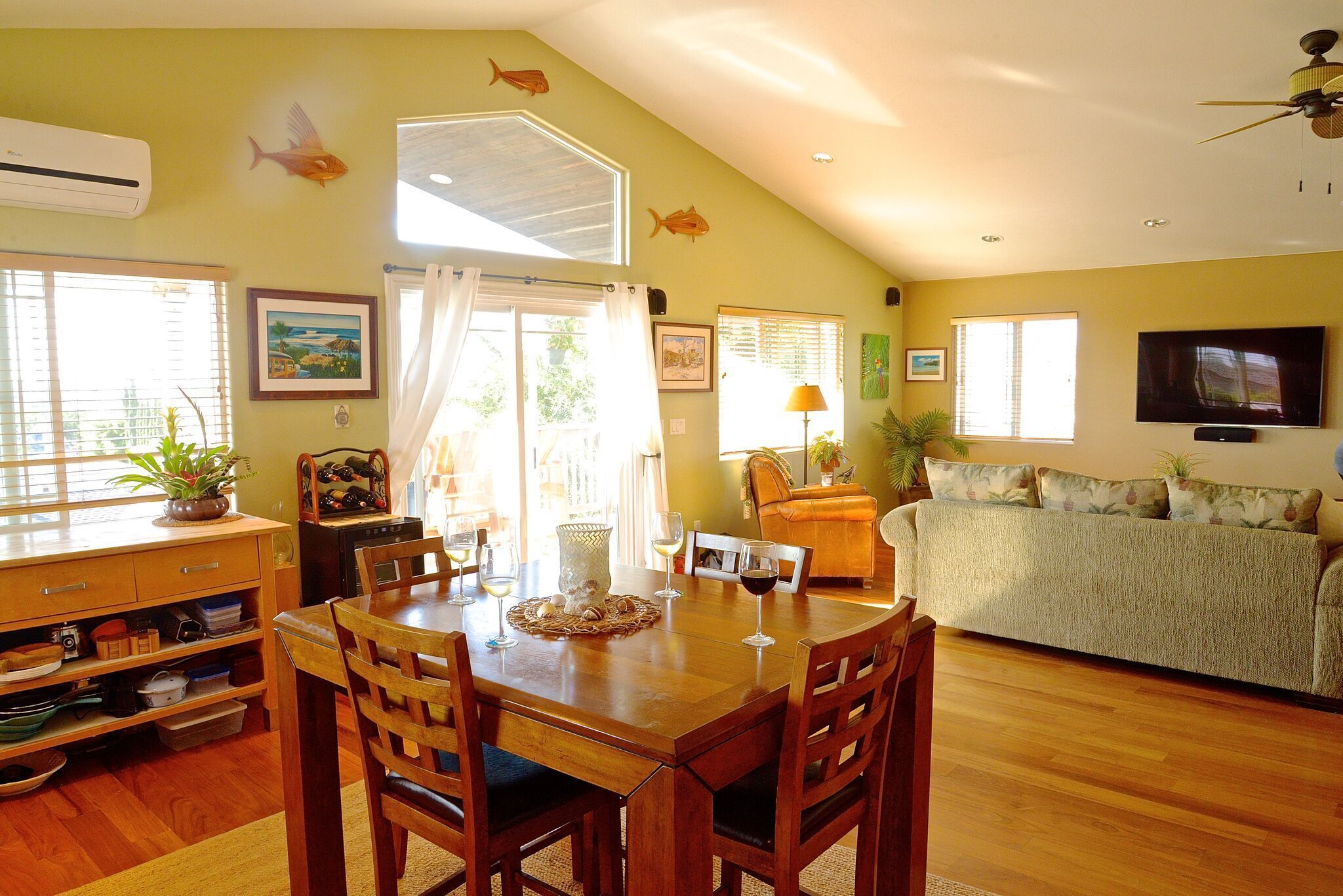 A dining area with a wooden table and chairs, a kitchen with a stove and cabinets, and a living area with a couch and TV.
