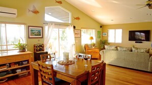 A dining area with a wooden table and chairs, a kitchen with a stove and cabinets, and a living area with a couch and TV. - Roomy, Quaint, Studio Loft w/ Bay View - Central SD Location  (San Diego)