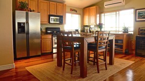 A kitchen with wooden cabinets, a stainless steel refrigerator, a microwave, and a dining area with a table and chairs. - Roomy, Quaint, Studio Loft w/ Bay View - Central SD Location  (San Diego)