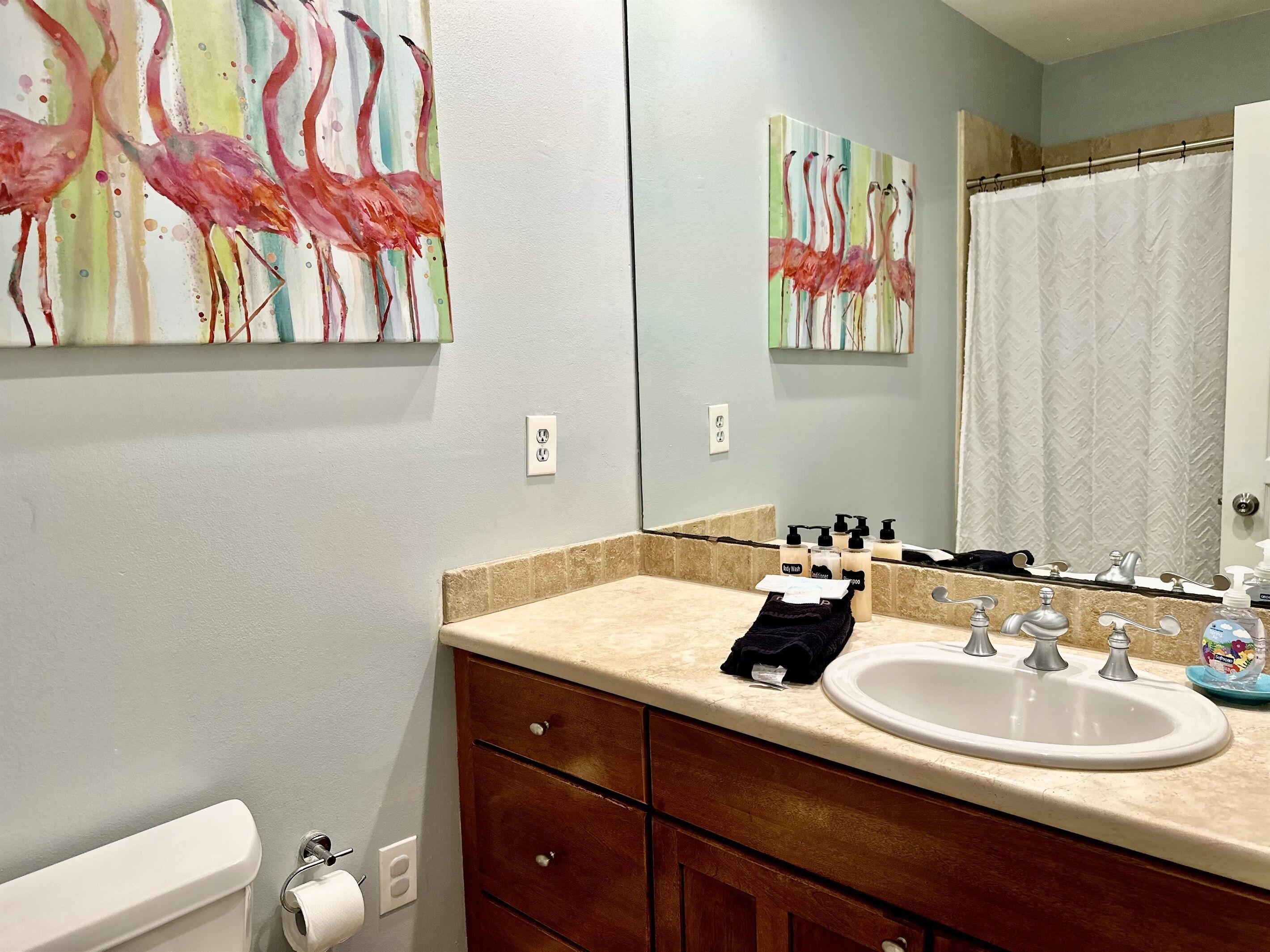 A bathroom with a beige countertop, a white sink, wooden cabinets, and two wall-mounted paintings of flamingos.