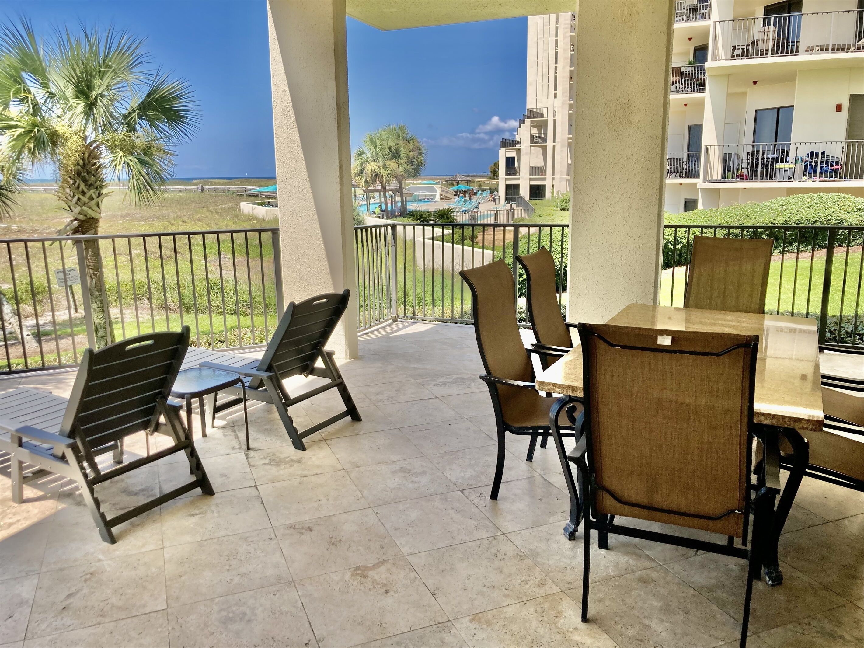 A balcony with a table and chairs, overlooking a pool and a building with balconies.