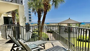 A balcony with two lounge chairs and a small table, overlooking a pool area and a building with balconies.