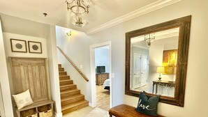 A hallway with a wooden bench, a large mirror, and a staircase leading to another room.