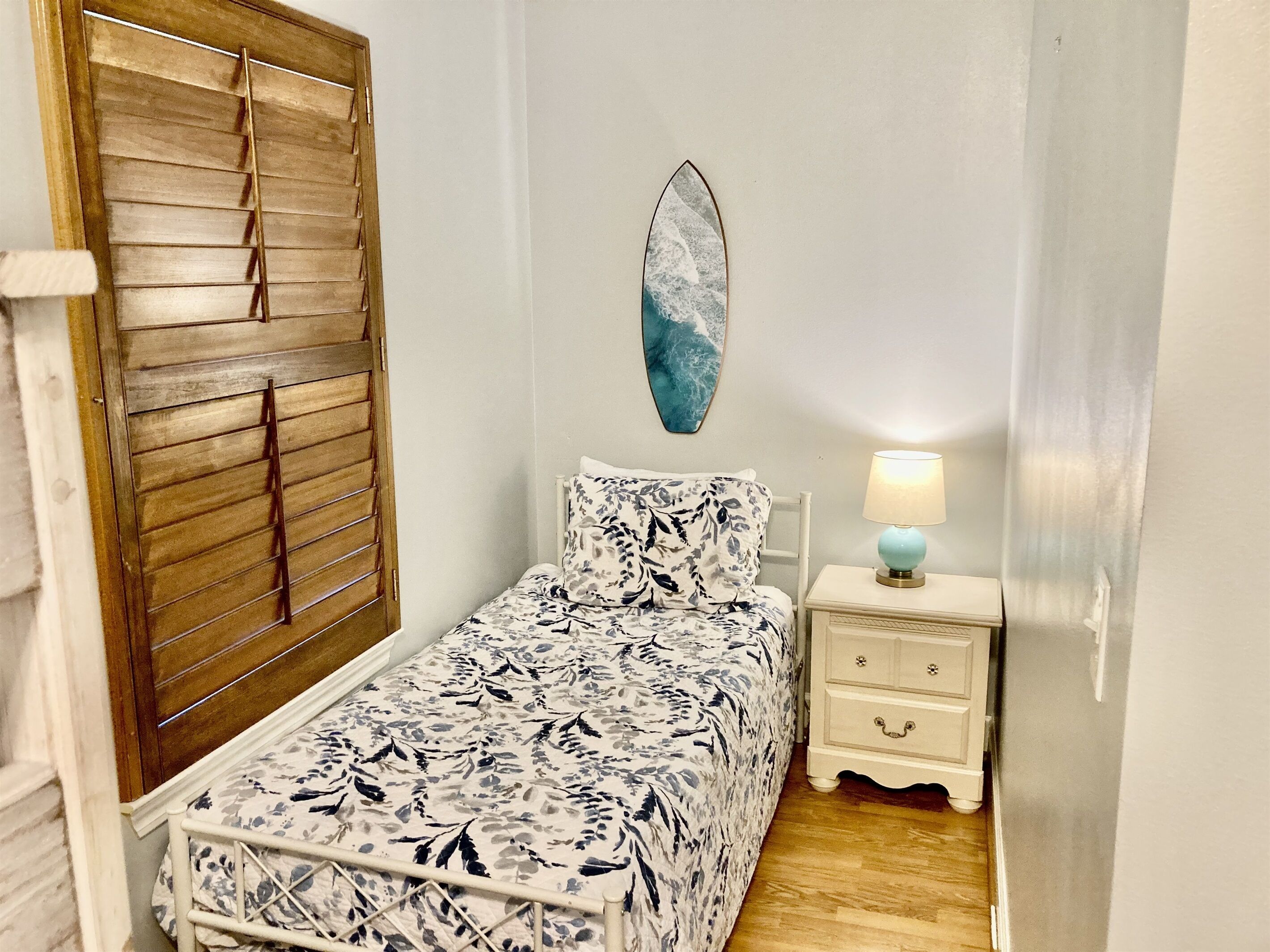 Een slaapkamer met een bed, een nachtkastje, een lamp, een houten deur en een aan de muur hangend schilderij.