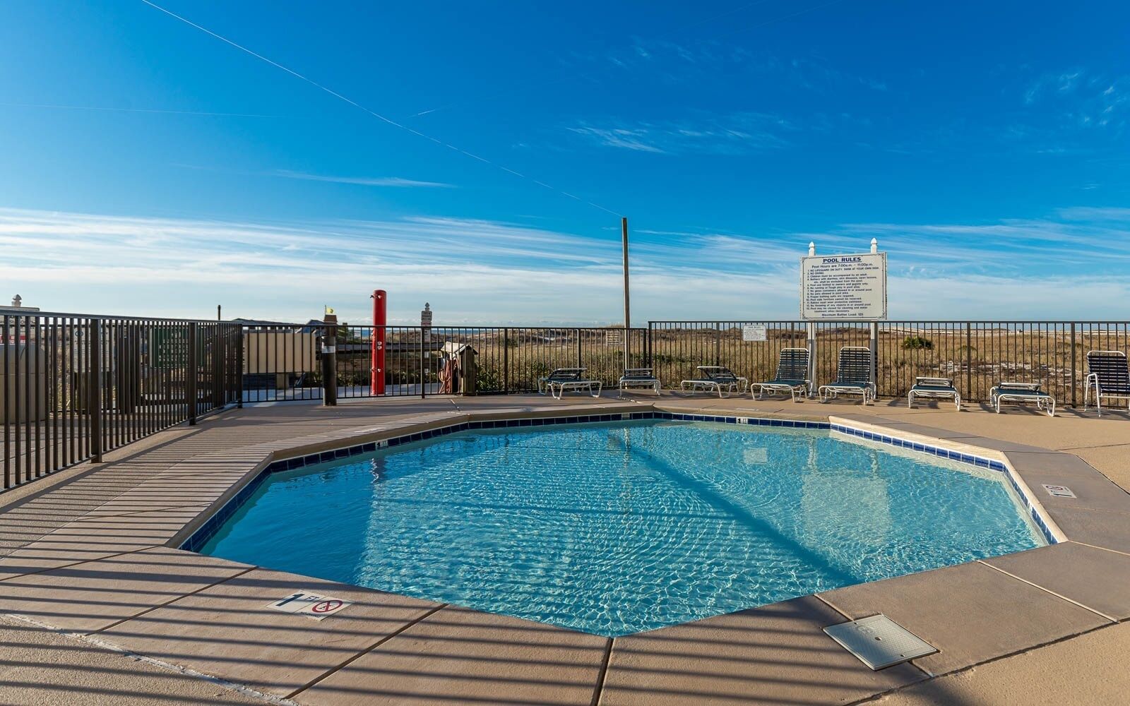 Ein rechteckiger Pool mit einer gefliesten Kante, umgeben von einem Metallzaun und einem Schild mit Poolregeln.