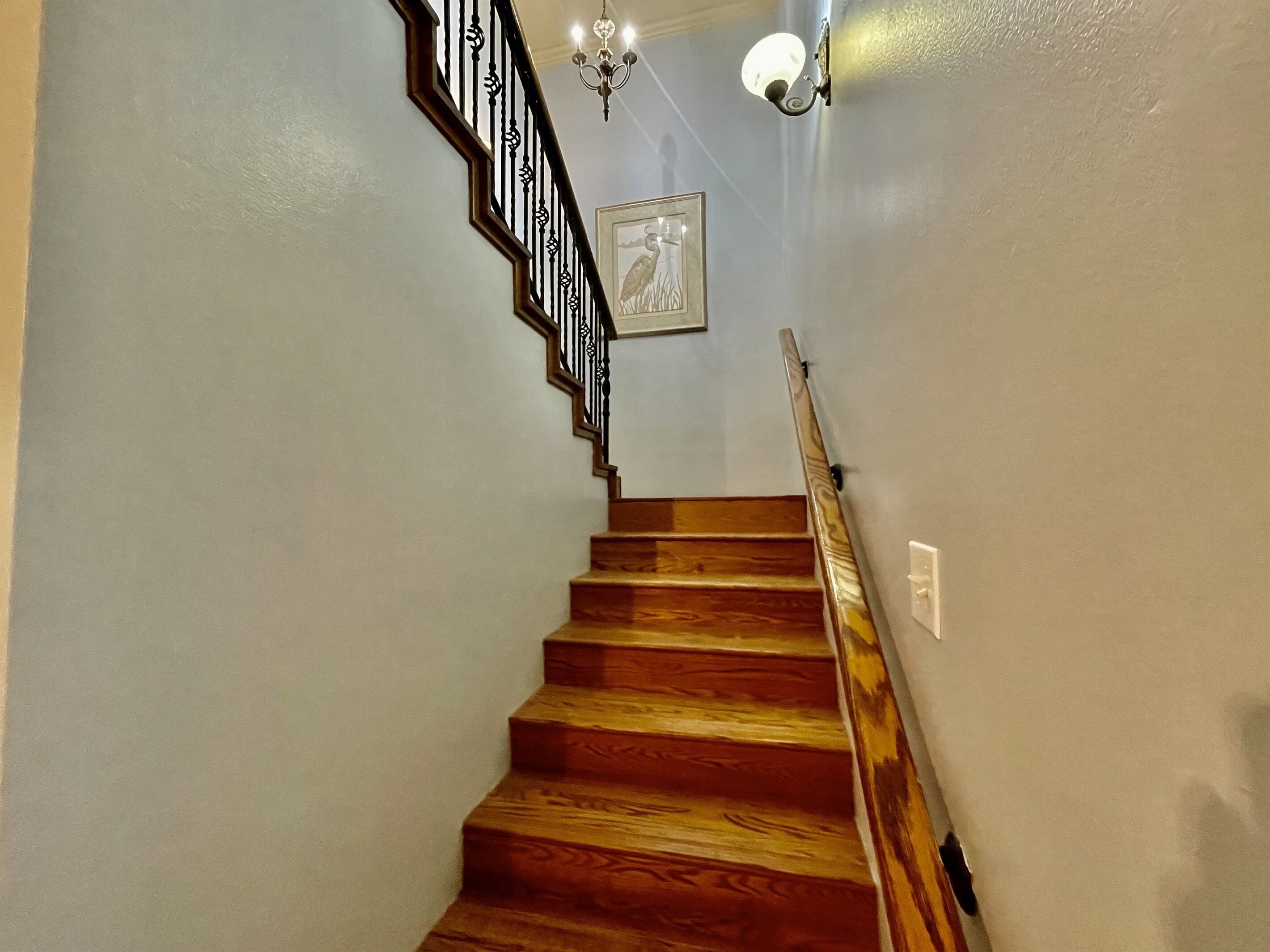 A wooden staircase with a black railing and a chandelier.