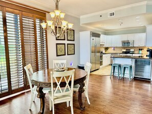 A dining area with a wooden table and chairs, a chandelier, and a kitchen with white cabinets and appliances.
