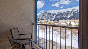 Un balcone con una sedia, vista su un paesaggio montano innevato e edifici residenziali.