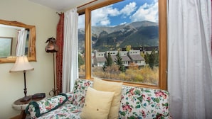 Una stanza con un'ampia finestra vista montagna, un divano floreale, una lampada e uno specchio.