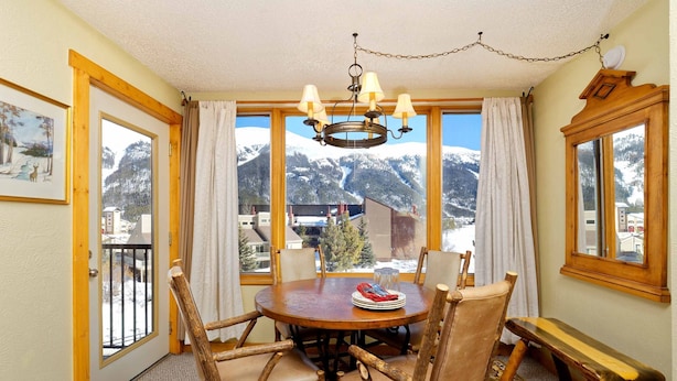 Zona pranzo con tavolo e sedie in legno, un lampadario e vista sulle montagne innevate.