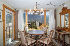 A dining area with a round table and chairs, a chandelier, and a view of mountains through large windows. - Best Value for Your Money in Ctr Vlg! Gorgeous Sky Chutes view. Free Pkg & WiFi (Copper Mountain)