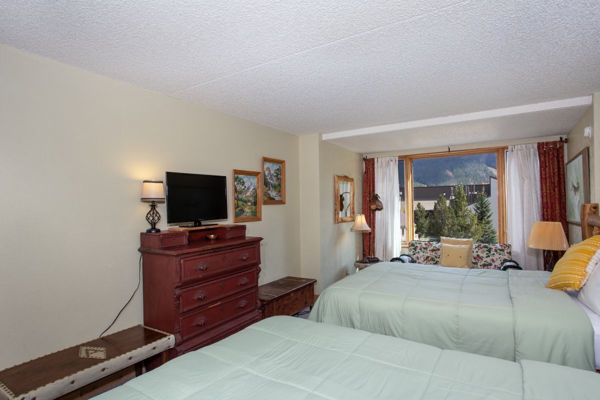 Hotelkamer met twee bedden, een televisie, een dressoir en een raam met uitzicht op de bergen.