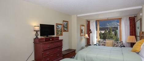 Hotelkamer met twee bedden, een televisie, een dressoir en een raam met uitzicht op de bergen.