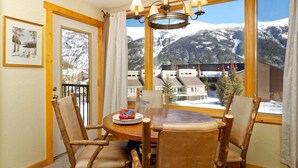 Un'area pranzo con sedie in legno e un tavolo, ampie finestre con vista sulle montagne e un lampadario.
