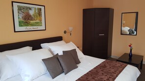 A hotel room with a bed, a wardrobe, a nightstand, a vase with flowers, and a framed picture on the wall.