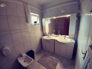 A bathroom with two sinks, a bidet, a mirror, and a small window with a curtain.