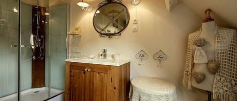 Un baño con cabina de ducha de vidrio, tocador de madera y un espejo redondo con apliques de pared.