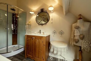 Een badkamer met een douchecabine van glas, een houten wastafelmeubel en een ronde spiegel met wandlampen.