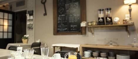 A dining area with a table set for breakfast, including plates, glasses, and a pitcher of orange juice. There are shelves with dishes and a chalkboard menu on the wall.