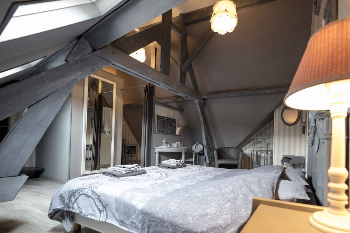 Een slaapkamer met een groot bed, een bureau en een stoel. Er is een raam en een lamp.